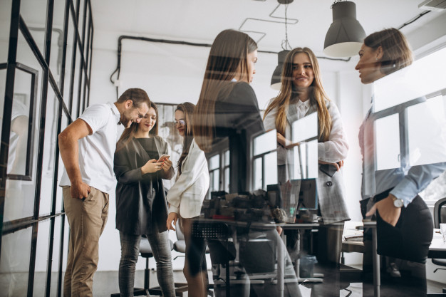 Groupe de personnes discutant dans un bureau, devant des vitrines et du matériel, sourires et échanges professionnels.